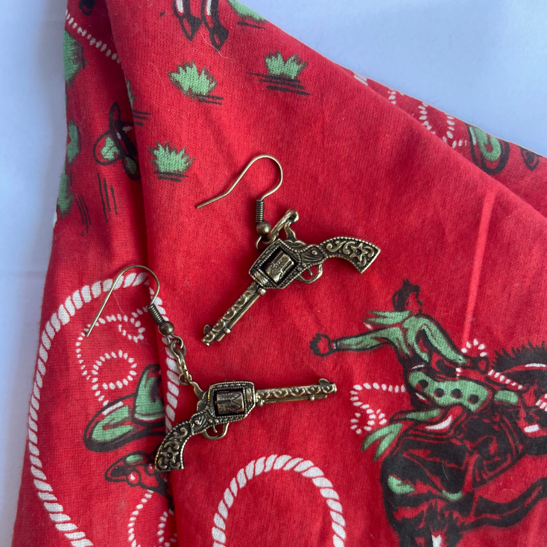 Close-up of unique spinning chamber mechanism on bronze revolver earrings styled with a vintage western outlaw style bandana