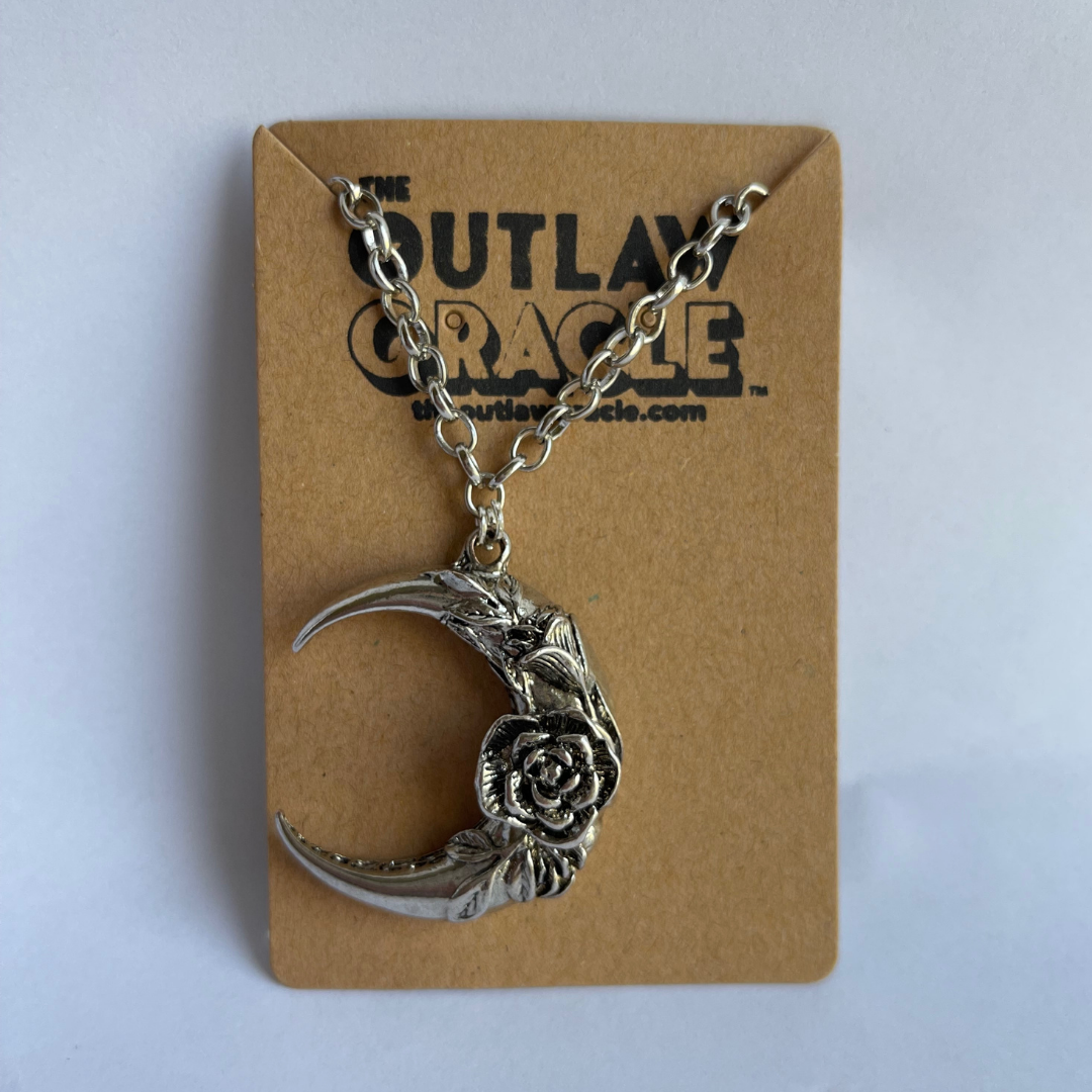 Detailed view of witchy moon charm showing rose design and silver patina on display card