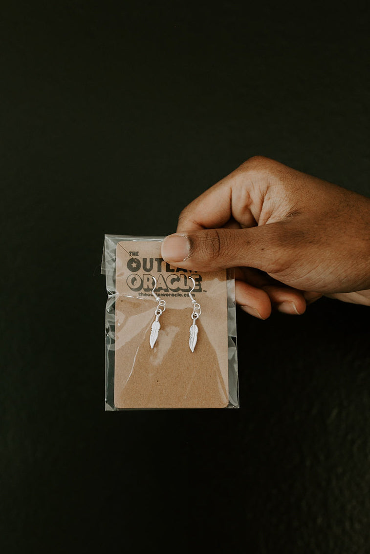 Tibetan silver feather dangle earrings featuring intricate plume detail and antique finish as shown on display card.