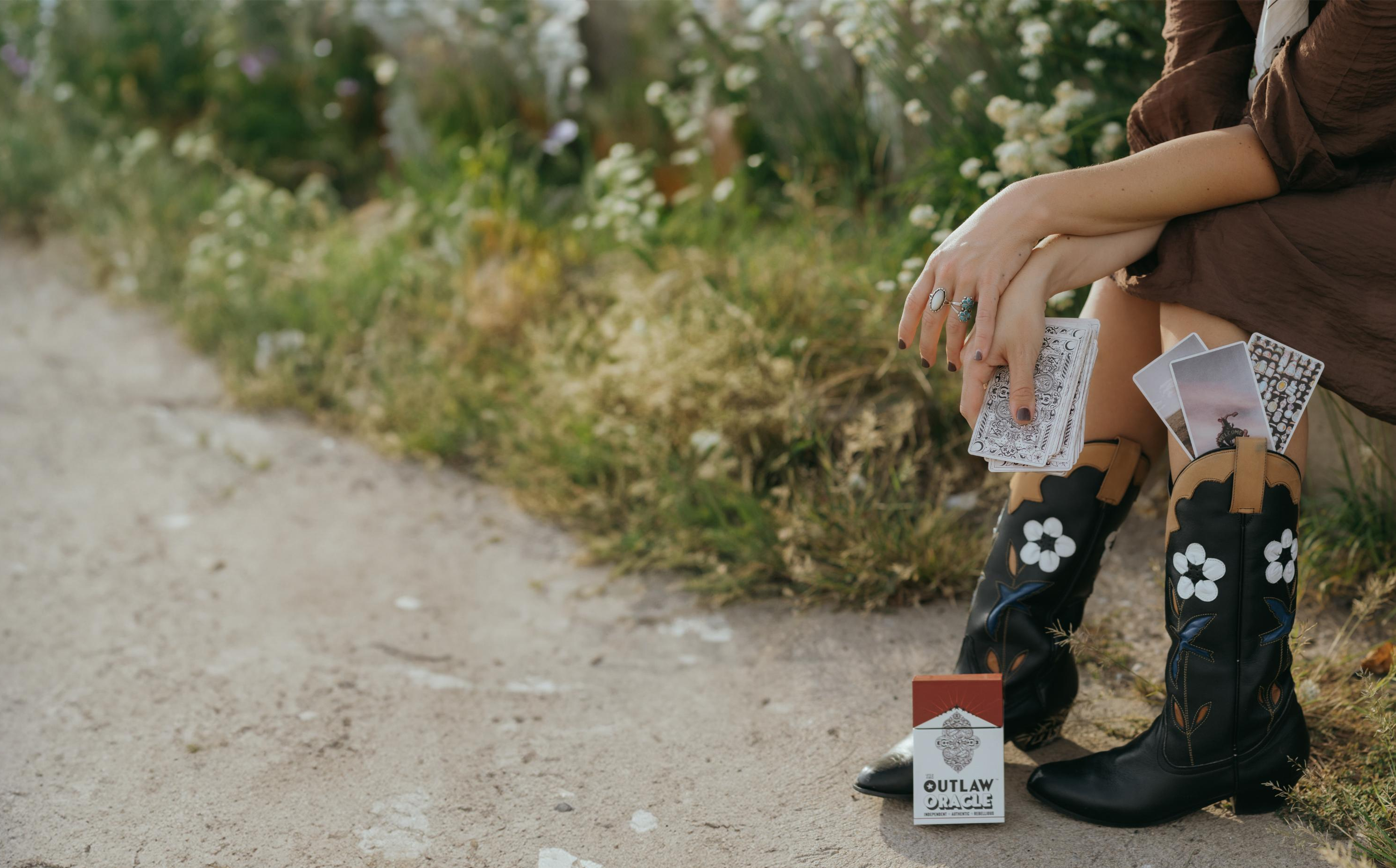 Woman in cowboy boots holding the outlaw oracle oracle cards and card case