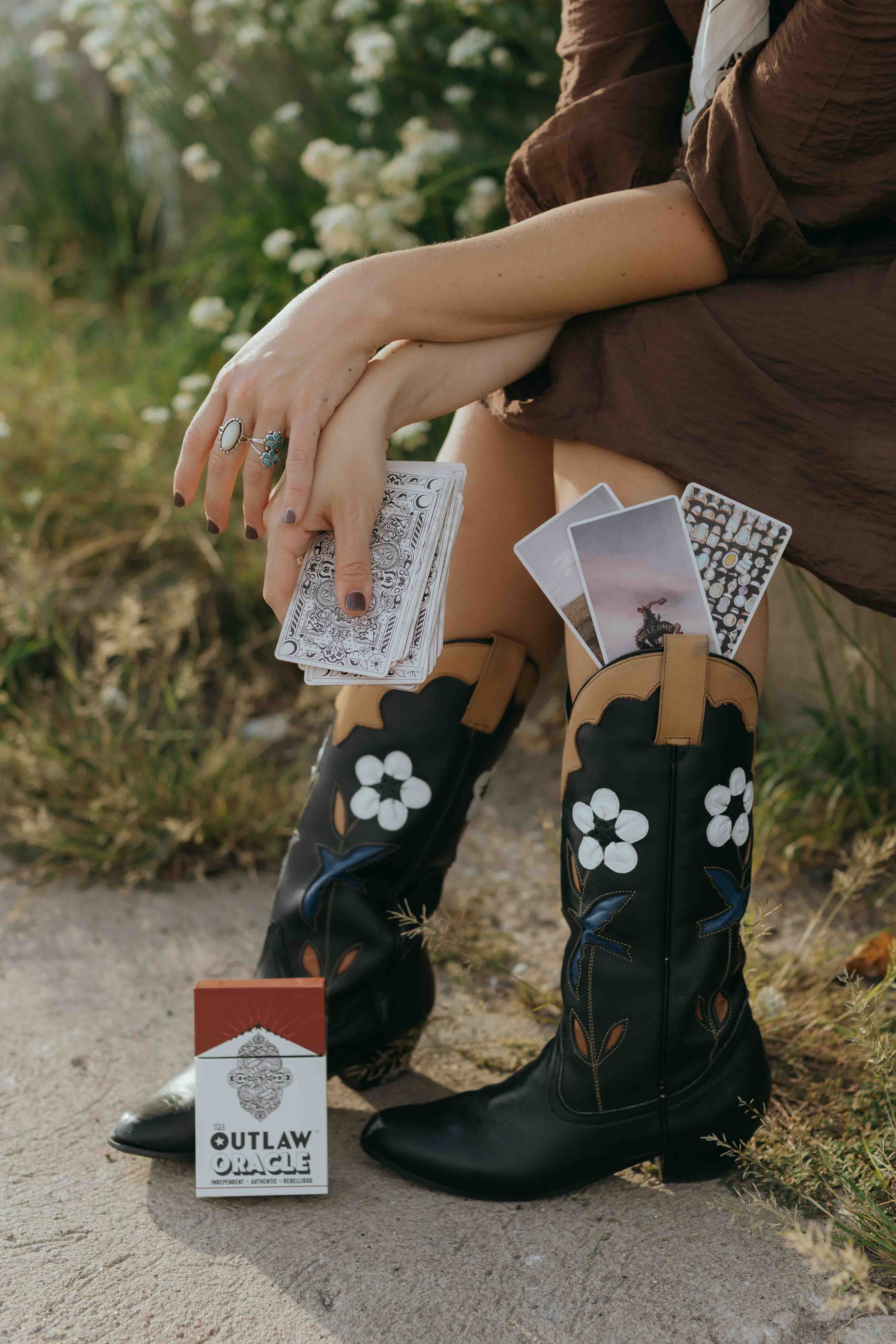 Outlaw Oracle cards and card deck styled with Western Fashion - showing the nostalgic red and white American Western inspired box that the oracle deck comes in, and the high quality oracle card stock in hand.  Beautiful quality and finish.  Looks great on your coffee table. 